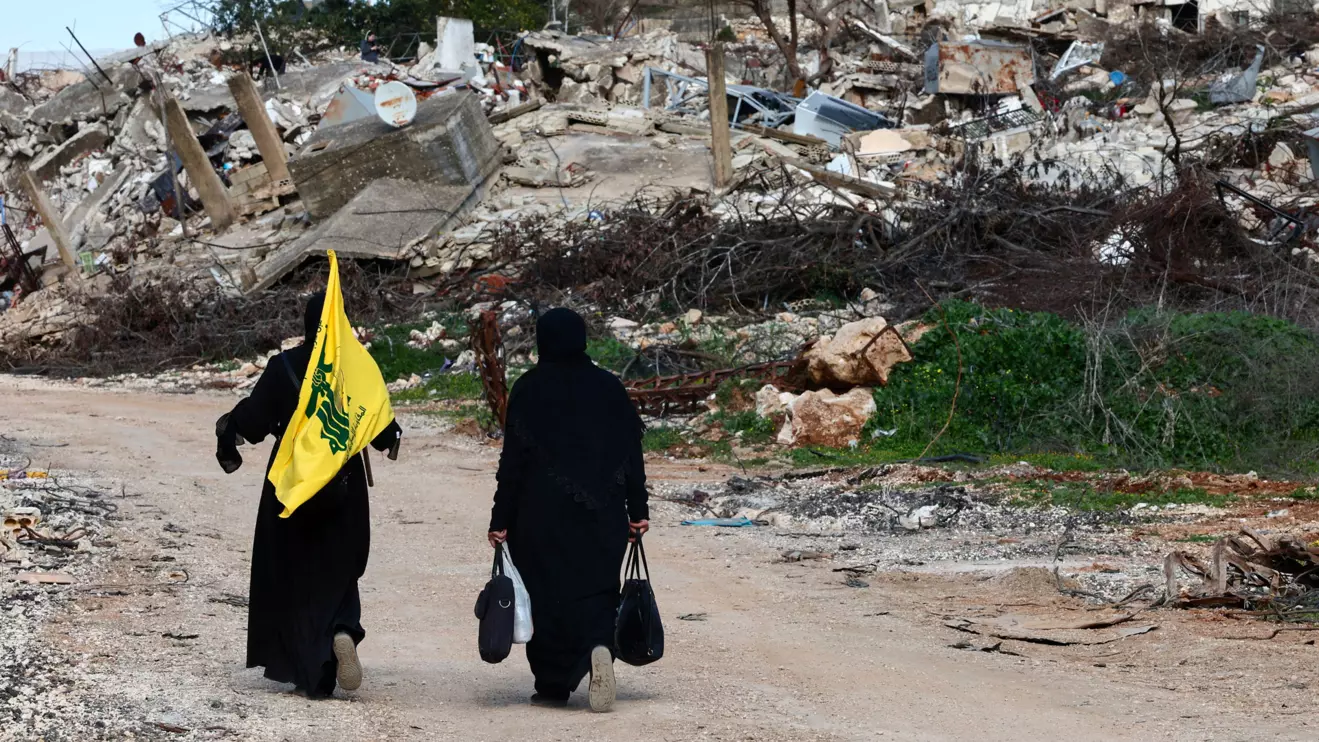 Women walk near destroyed buildings, with one holding the flag of Hezbollah, in the southern Lebanese village of Kfar Kila, Reuters/Emilie Madi