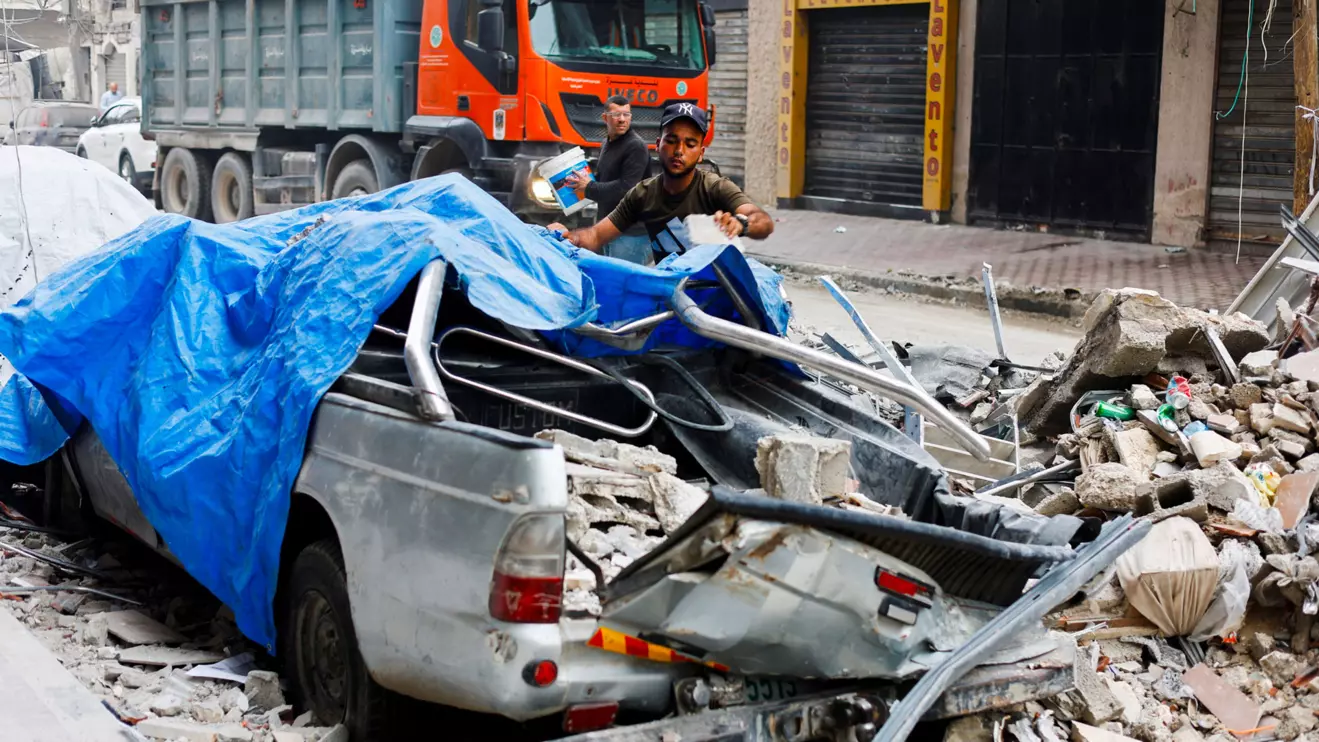 A Palestinian man moves debris next to a destroyed vehicle as he inspects the site of an Israeli airstrike on a residential building on Tuesday, in Gaza City, May 27, 2026. Reuters/Mahmoud Isaa