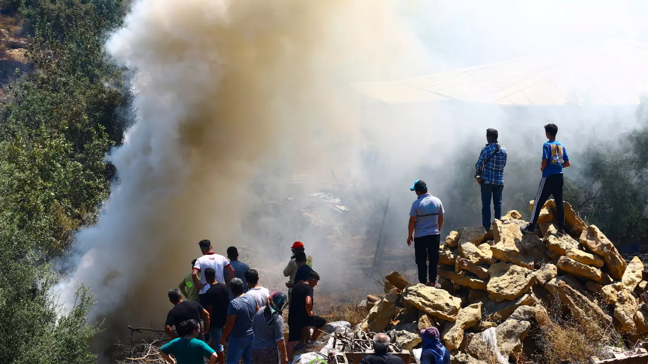 People stand next to smoke rising from the wildfire in the Aksu district of Antalya, a Mediterranean city in southern Turkey, July 25, 2025. Reuters/Kaan Soyturk