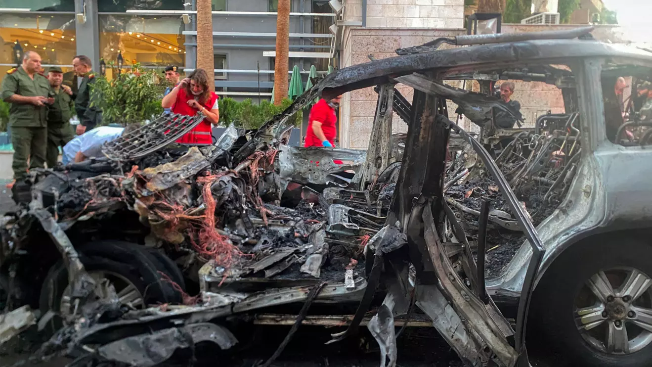 People stand near the wreckage of a car after what the Syrian state television said was a "guided missile attack" on the car in the Mazzeh area of Damascus, Syria October 21, 2024. Reuters/Firas Makdesi