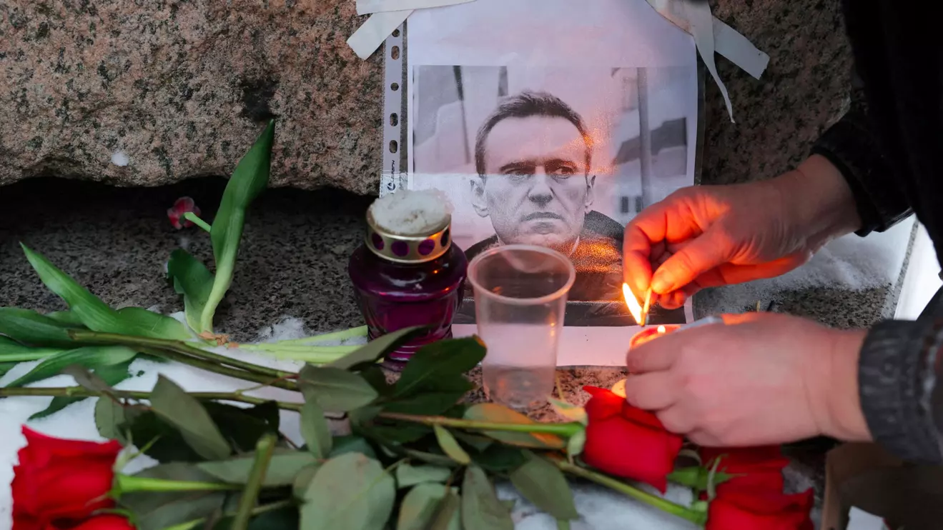 A person lights a candle next to a portrait of Russian opposition leader Alexei Navalny at the monument to the victims of political repression following Navalny's death, in Saint Petersburg, Russia, February 16, 2024, Reuters