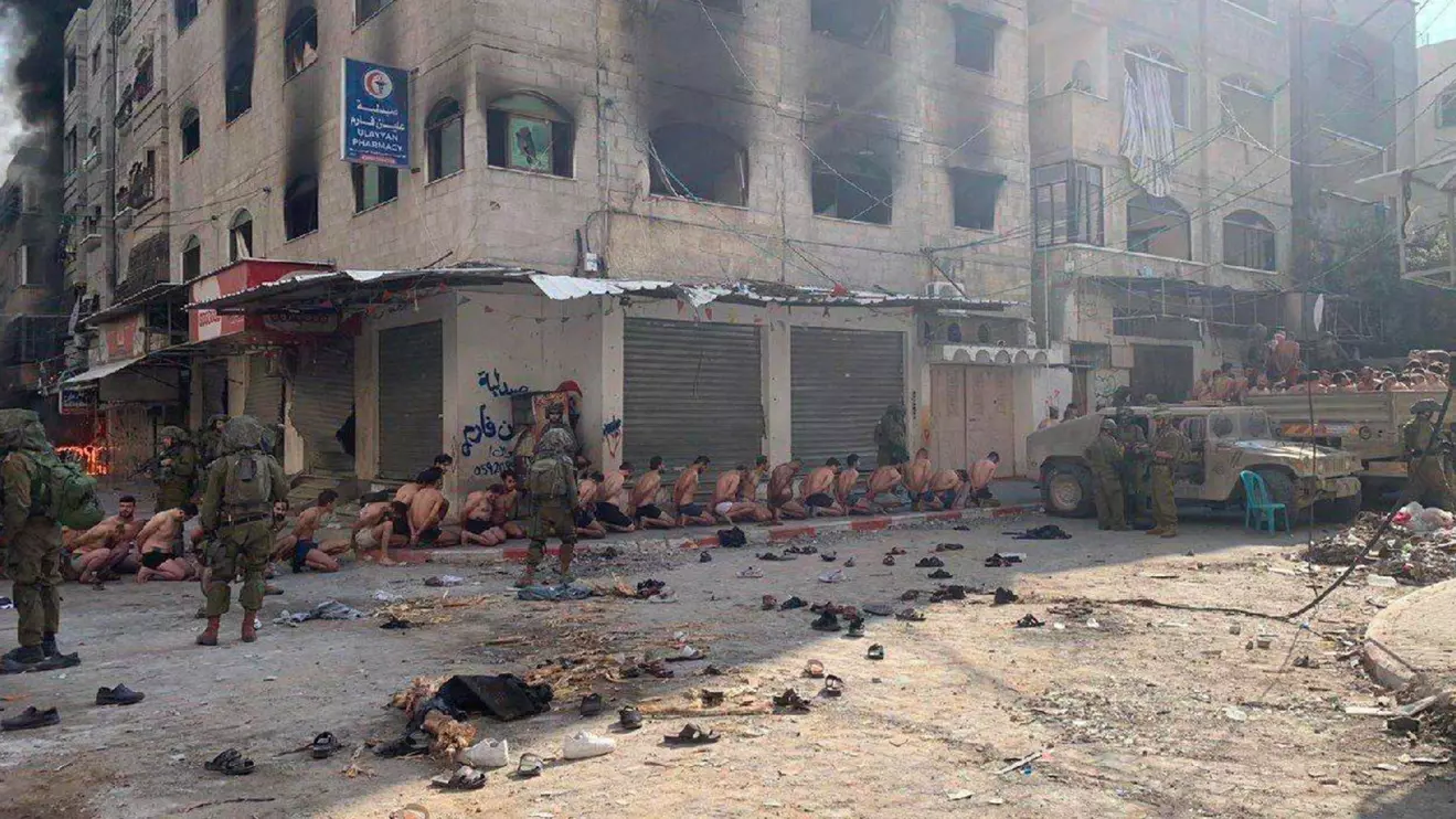 Captured and detained Palestinians sit on a street in Beit Lahia, northern Gaza Strip, as Israeli soldiers stand guard © Reuters 