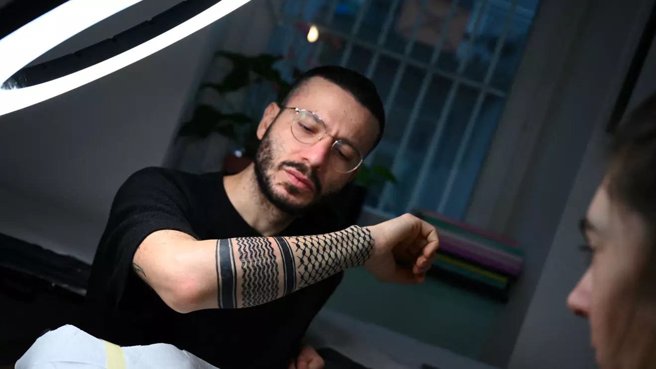 Palestinian Syrian poet Ramy Al-Asheq, 34, looks at his forearm which is tattoed with the black-and-white chequerboard pattern of the Palestinian keffiyeh by tattoo artist Tana Torr in Berlin, Germany Reuters/Annegret Hilse