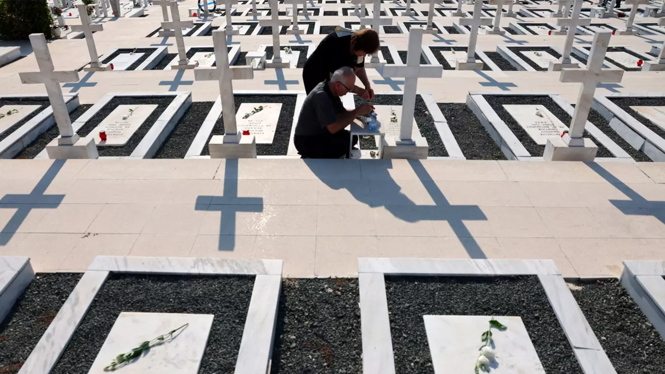 Relatives sit next to the graves of soldiers killed in the 1974 Turkish invasion of Cyprus at the Tymvos Makedonitissas military cemetery in Nicosia, Cyprus July 20, 2025. Reuters/Yiannis Kourtoglou