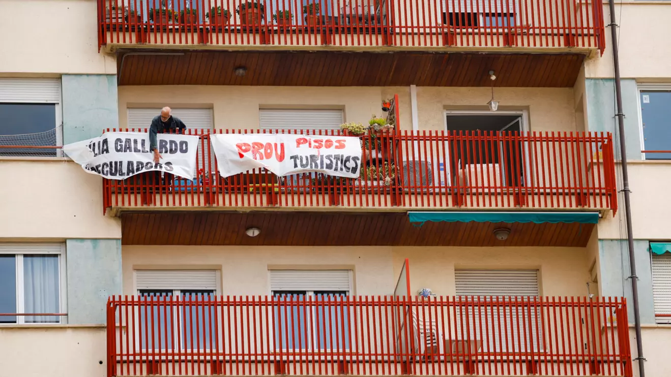 A man ties protest banners in the balcony of a building that was recently converted for tourist use at Sants neighborhood in Barcelona, Spain, May 19, 2023. The banner reads "No more tourist flats". Reuters/Albert Gea