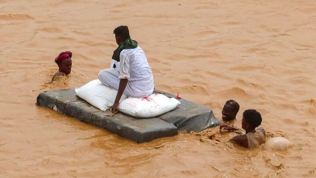 A person sits on bags of aid on a makeshift raft while others wade through flood water, following devastating floods, in South Tokar, Red Sea State, Sudan, August 28, 2024. Reuters/El Tayeb Siddi