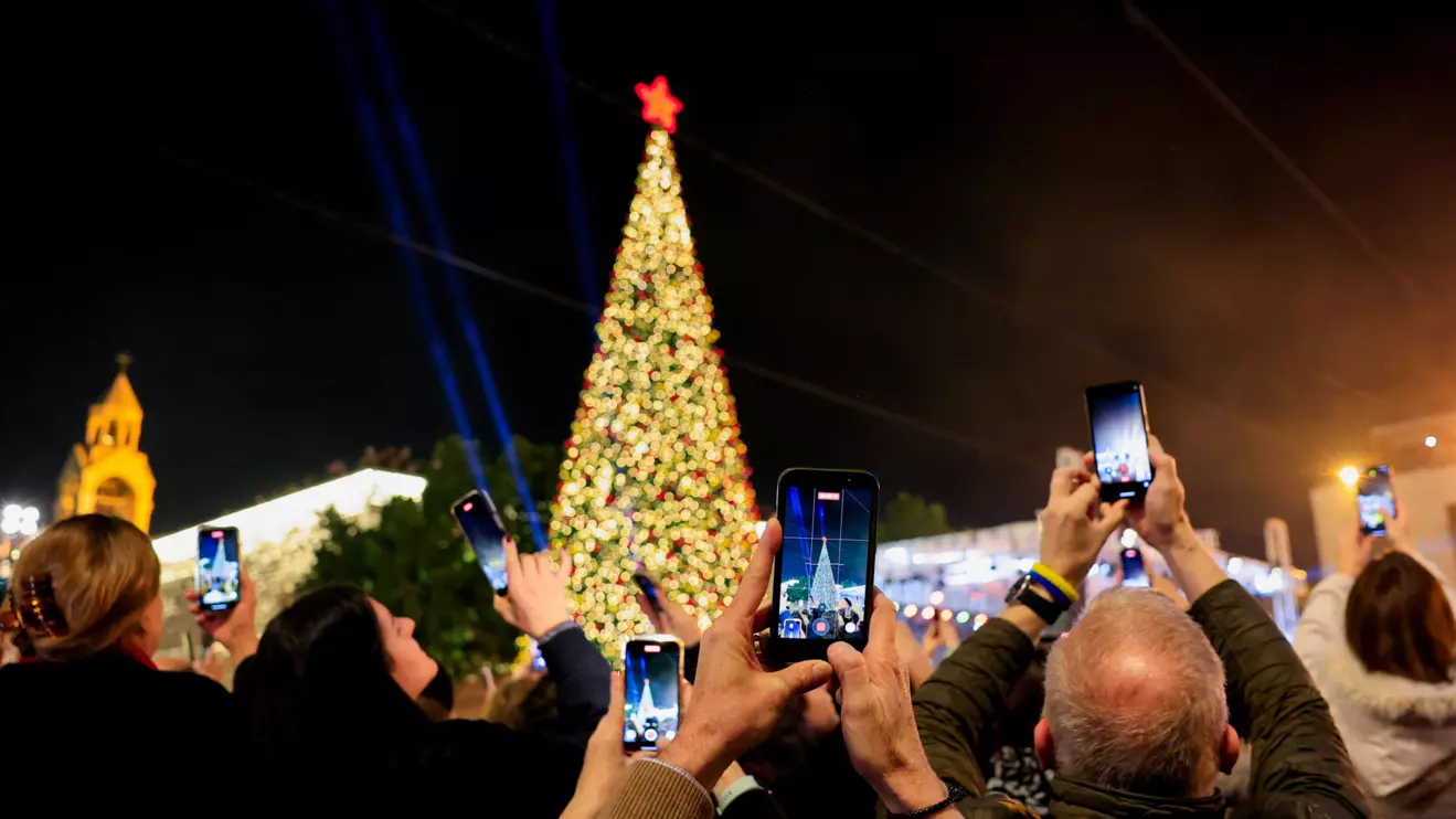 Palestinians use phones to record as a Christmas tree is lit up in Manger Square outside the Church of the Nativity, in Bethlehem, December 6, 2025. Reuters/Mussa Qawasma