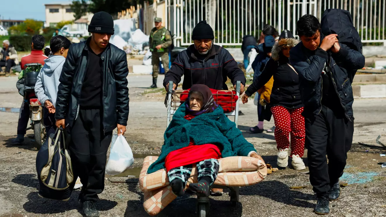 A man pushes an elderly woman on an airport luggage trolley at Hmeimim Air Base, in Latakia, western Syria, March 20, 2025. Thousands of Alawite families sought refuge there after deadly attacks by pro-government forces targeting their villages. A Reuters investigation found the violence left nearly 1,500 people dead, Reuters