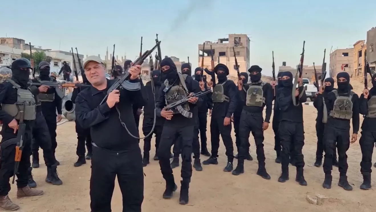 The head of an anti-Hamas faction, Hussam Alastal, fires a weapon in the air as he is surrounded by masked gunmen, in an Israeli-held area in Khan Younis, in the southern Gaza Strip, in this screenshot taken from a video released November 21, 2025. Hussam Alastal