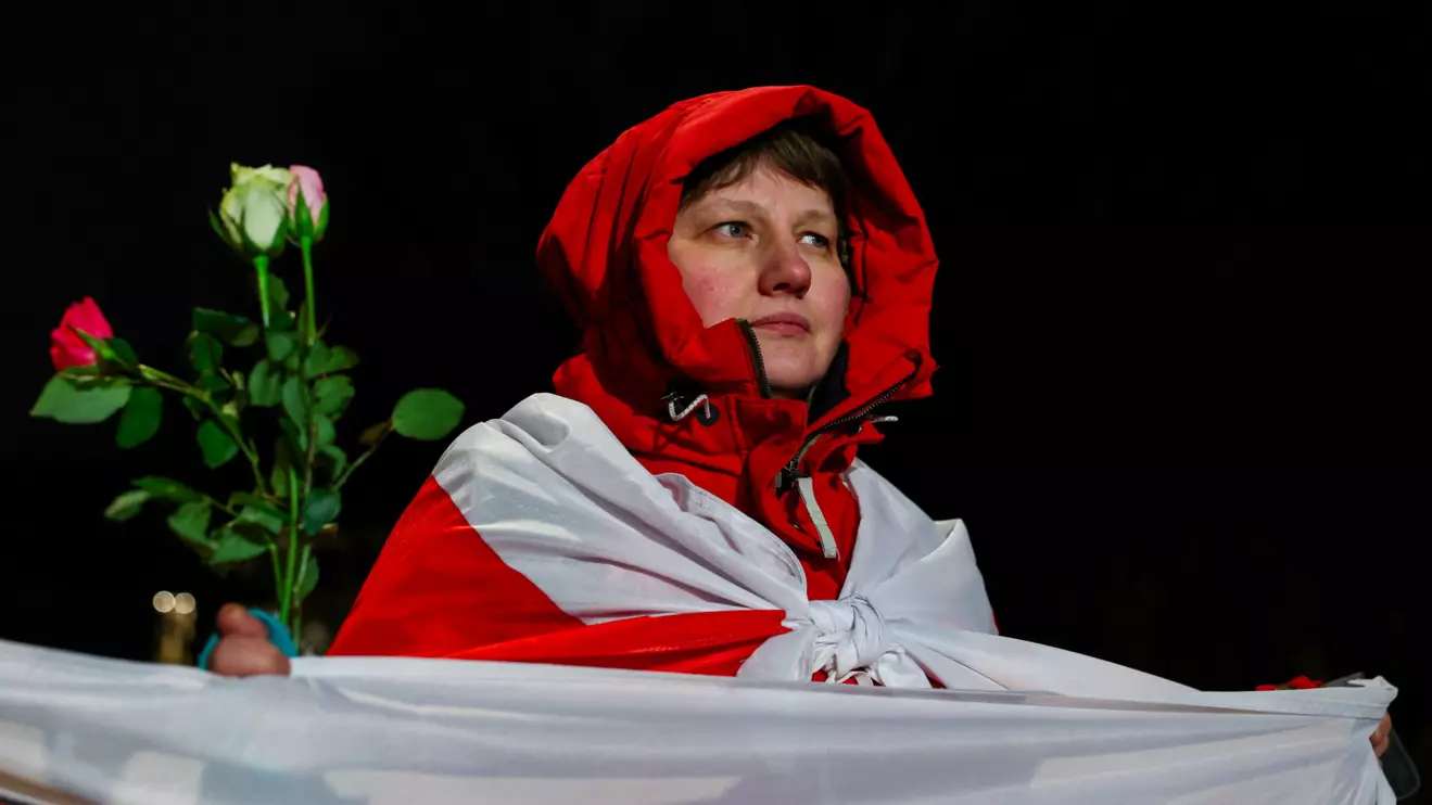 A woman holds a flag in the colours of a historical Belarusian flag and flowers as people gather waiting outside the U.S. embassy, on the day of the arrival of prisoners released from Belarus, in Vilnius, Lithuania, December 13, 2025. Reuters/Gonzalo Fuentes