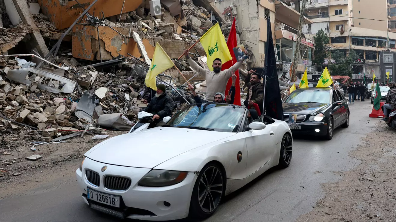 Men carry Hezbollah flags and a picture depicting late Hezbollah leader Sayyed Hassan Nasrallah as they drive past damaged buildings at the entrance of Beirut's southern suburbs, after a ceasefire between Israel and Hezbollah took effect, Lebanon November 27, 2024. Reuters/Mohamed Azakir