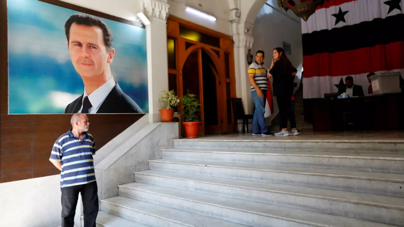 A man stands in front of a poster depicting Syria's President Bashar al-Assad at a polling station, during parliamentary elections in Damascus, Syria July 15, 2024. Reuters/Yamam al Shaar